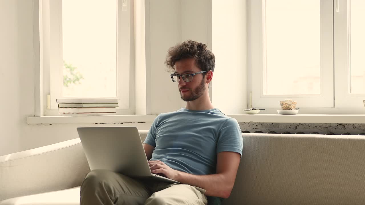 戴眼镜的年轻男性像沙发一样坐在笔记本电脑上