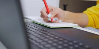 一个专心致志的十几岁女孩正坐在家里的笔记本电脑屏幕前做作业。对笔记本记录的特写。