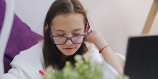 戴眼镜的一名女小学生正在利用互联网进行家庭教育。远程学习。