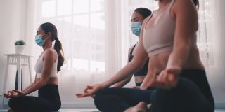 一群戴着医用口罩在健身房做瑜伽的亚洲女性。