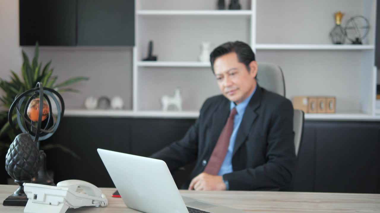 照片中的亚洲最高经理坐在办公室里，微笑着看着镜头