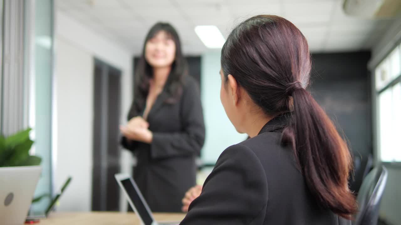 一位年轻的亚洲女员工正在聆听专业培训师的演讲，讲解营销策略。有技能的教练在办公室里教育不同的同事。