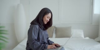 4k, Portrait，一个可爱的亚洲少女。穿着灰色衬衫躺在床上，带着笔记本电脑在卧室里开心地上网学习