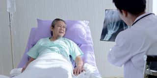 亚洲男医生手持骨x光片与患者交谈，讲解治疗方法，鼓励老年亚洲男患者术后
