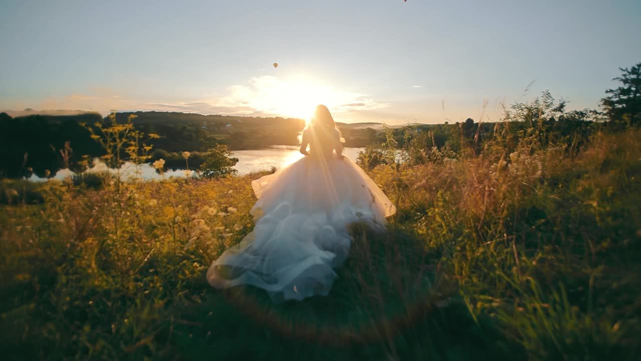 美丽的新娘在夕阳的映衬下奔向湖边。莫兰朗日的日落和背光的光线。年轻女子在长雪纺连衣裙