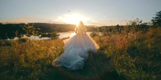 美丽的新娘在夕阳的映衬下奔向湖边。莫兰朗日的日落和背光的光线。年轻女子在长雪纺连衣裙