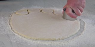 一个女人把生面团切下来做小圆面包，甜甜圈。