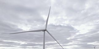 旋转风车在阴天背景。无人机俯瞰，清洁的可再生能源由风力涡轮机产生。在海上或野外的大农场全速旋转叶片。另一种生活方式