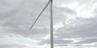 旋转风车在阴天背景。无人机俯瞰，清洁的可再生能源由风力涡轮机产生。在海上或野外的大农场全速旋转叶片。另一种生活方式