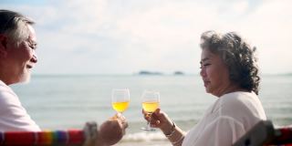 亚洲老年夫妇在夏天度假时在海滩上喝酒