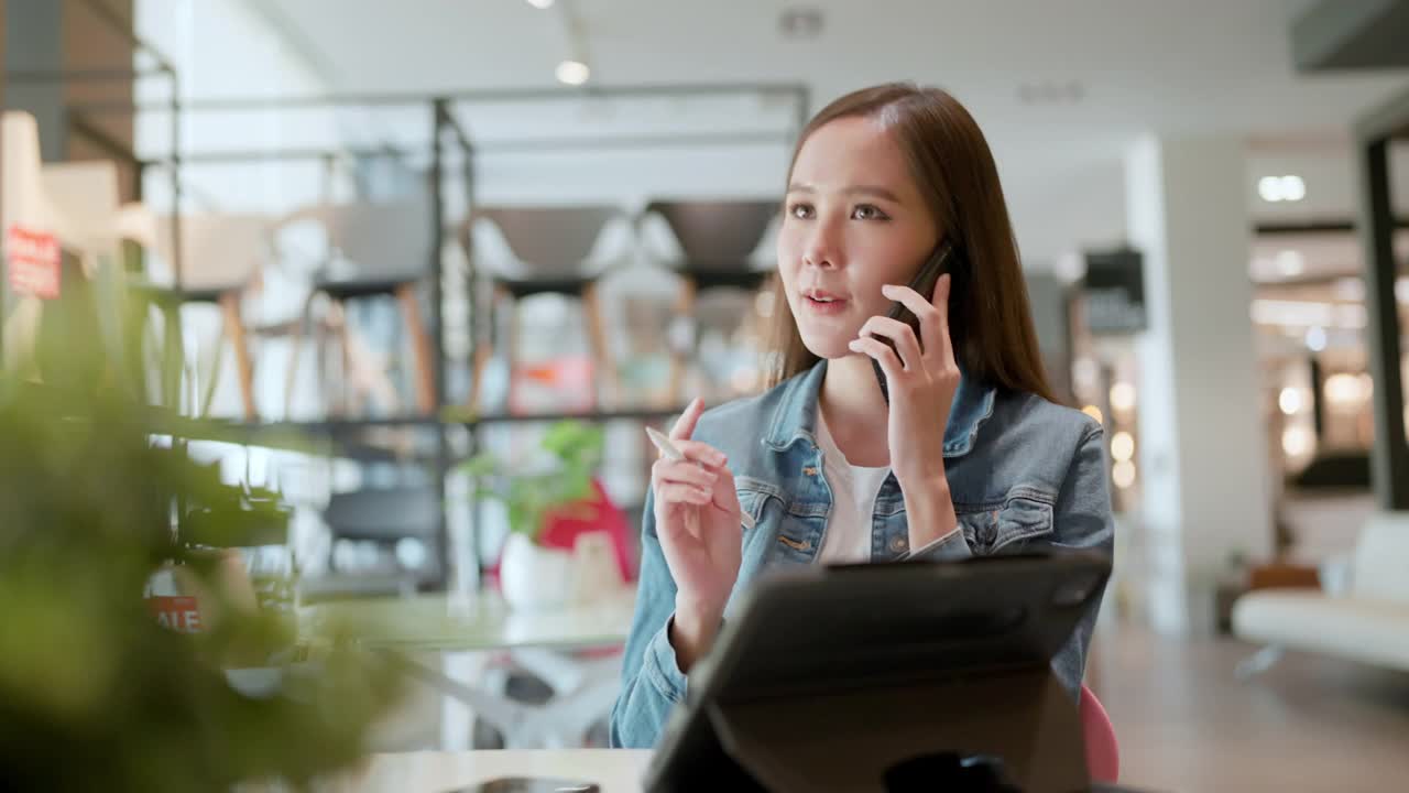 聪明的休闲亚洲女商人创业公司企业家小企业主工作和讨论与客户在新的商店商店办公室背景有吸引力的开朗的女性使用平板电脑智能手机