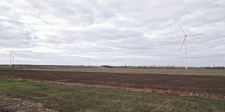 在田间的大农场全速转动叶片。旋转的风车在灰色的天空背景。由风力涡轮机产生的清洁可再生能源。另一种生活方式