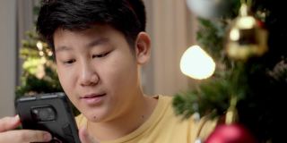亚洲男孩在圣诞节的灯光背景下，晚上在家玩手机游戏。