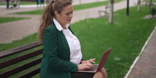 快乐超重的女商人坐在城市的长椅上聊天，在笔记本电脑上上网。肖像自信成功有吸引力的白人妇女在户外短信在线微笑。