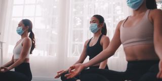 一群戴着医用口罩在健身房做瑜伽的亚洲女性。