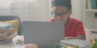 戴眼镜的聪明黑人男孩在笔记本电脑上做作业，一边学习一边玩