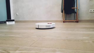 圆形白色机器人吸尘器正在打扫房间里的灰色层压板视频素材模板下载