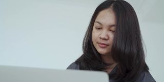 4k, Portrait，一个可爱的亚洲少女。穿着灰色衬衫，带着笔记本电脑在卧室的床上愉快地学习