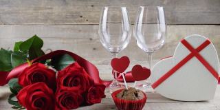 情人节。两杯香槟，红玫瑰，木制背景上的心形盒子。倒香槟。情人节。文本的地方