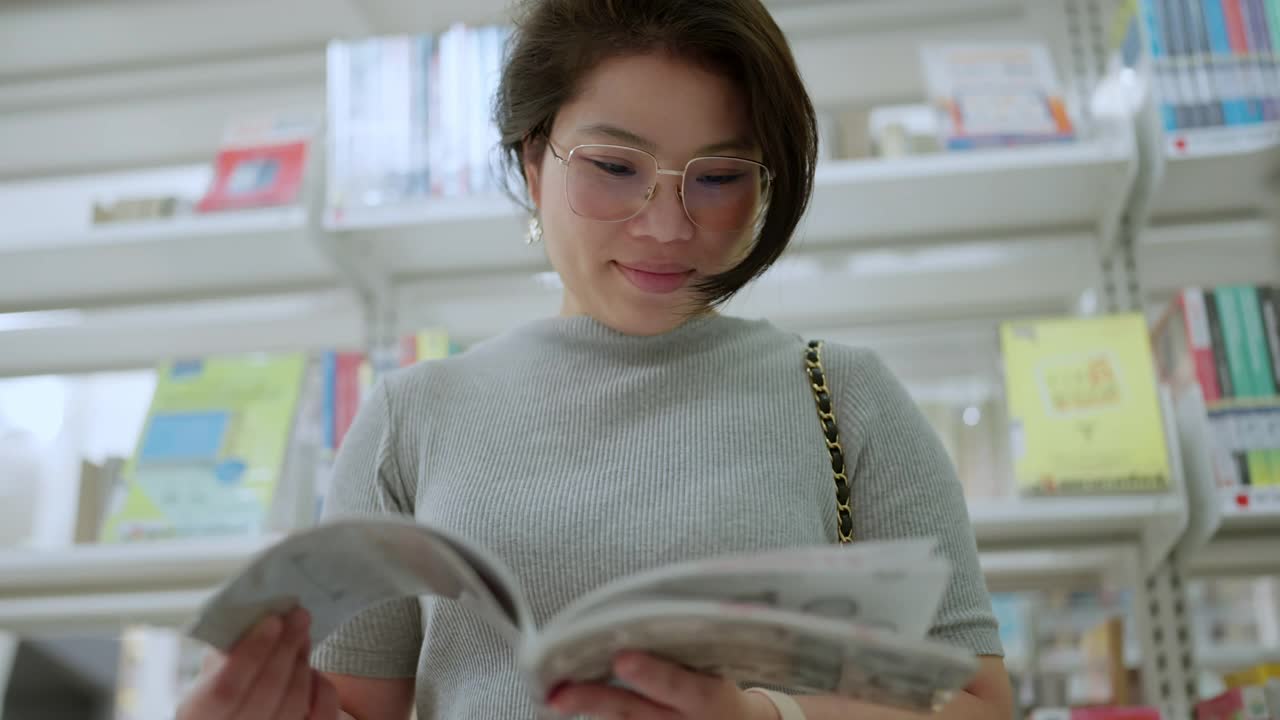 一位迷人的亚洲女性成年女性正在社区图书馆仔细地翻阅书籍。她穿着休闲装，正在看她感兴趣的书