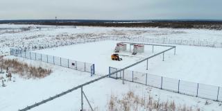 在油气田的针叶林上用小型装载机扫雪。石油和天然气工业在崎岖的北方地区。无人机绕着拖拉机飞