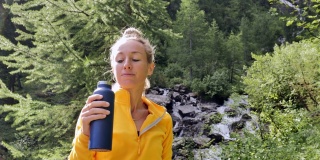 一个徒步旅行的女人从金属瓶子里喝新鲜的水。女性天然保湿。积极健康的生活方式。