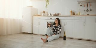 幸福的家庭的主人。年轻开朗的亚洲女人坐在厨房地板上，喝着葡萄酒，享受着她自己的公寓