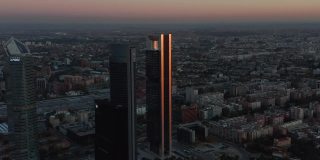 黄昏时分，Cuatro Torres商业区未来派摩天大楼的空中镜头正在下降。光滑的立面反映了彩色的黄昏天空