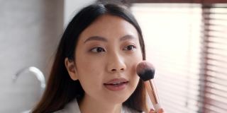 弥补。漂亮的亚洲女人用化妆刷在脸颊上涂腮红