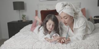 混合亚洲年轻女孩假装玩美甲美容沙龙与她的母亲在床上，家庭生活方式健康的概念