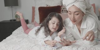 混合亚洲年轻女孩假装玩美甲美容沙龙与她的母亲在床上，家庭生活方式健康的概念
