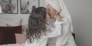 混合亚洲年轻女孩假装扮演化妆师，美容沙龙与她的母亲在床上，家庭生活方式健康的概念