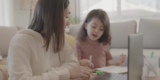 亚洲母亲帮助学龄前的女儿女孩在家里使用笔记本电脑电子学习，放大在线虚拟课堂，家庭教育，新常态的概念