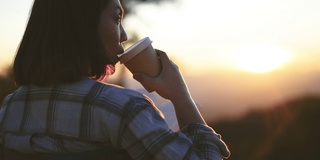 女人在户外，拿着咖啡杯在日落时分的山上放松