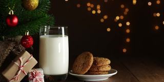 在圣诞树上放牛奶和饼干。圣诞老人手把带红丝带的礼盒放在木桌上