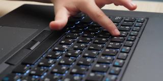 小男孩的手和手指按下笔记本电脑键盘上的按钮的特写视频。孩子在电脑键盘上打字。