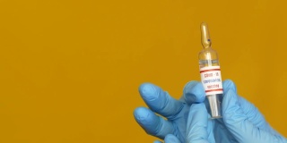 黄色背景下，戴着蓝色医用手套的医生手中的covid-19疫苗的特写镜头。含冠状病毒疫苗的安瓿疫苗试验阻止病毒有选择性的重点