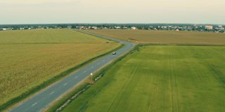 鸟瞰图的汽车SUV在运动的乡村道路通过夏季绿地。农业乡村田野乡村景观。年轻的小麦种植。汽车在快速移动