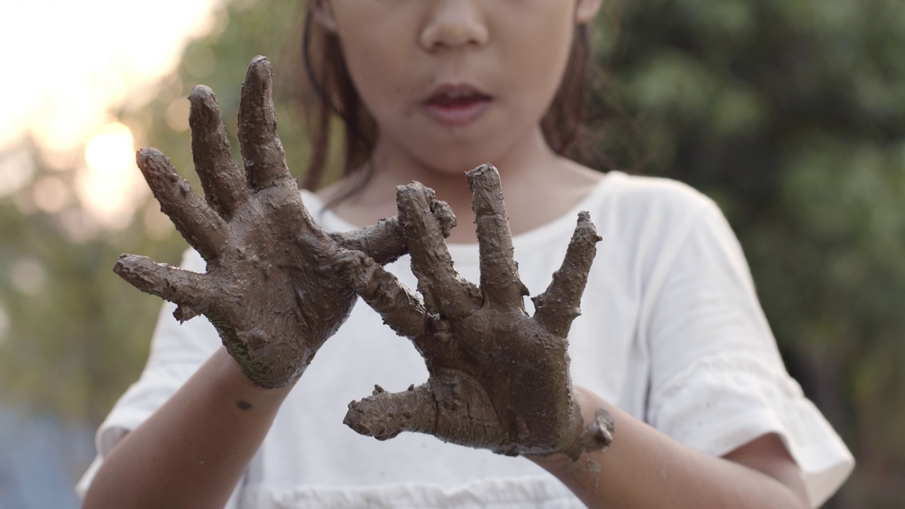 亚洲女孩在植树后玩泥巴和展示脏手