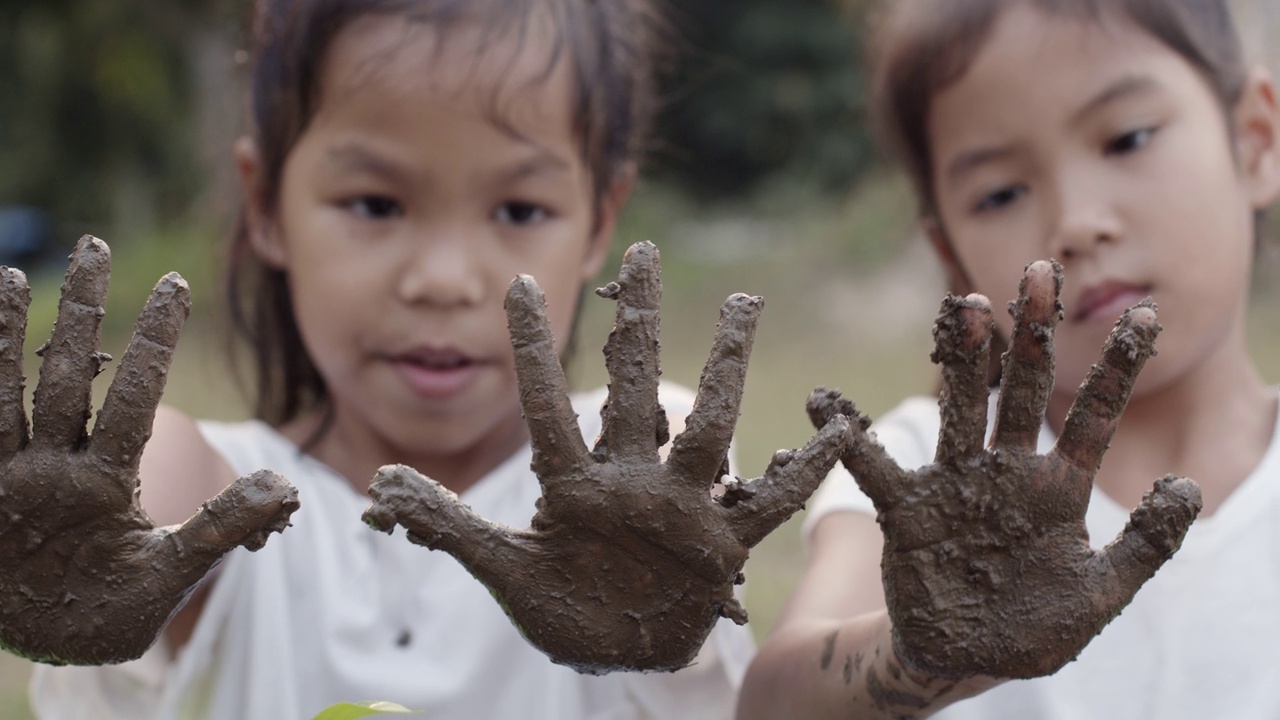 两个亚洲女孩玩泥巴和显示脏手后种植