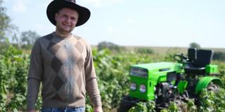 一个自豪的年轻农民站在他的绿色拖拉机前。
