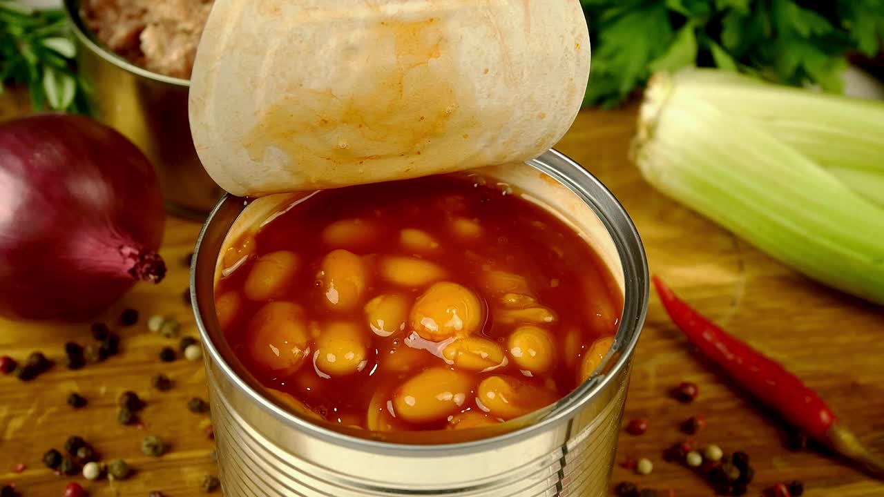 厨师用汤匙从厨房木板上的金属罐中取出番茄酱炖豆。