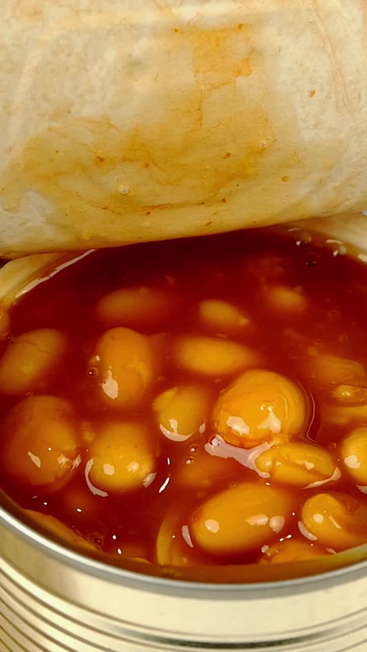 勺子从金属罐头里取出番茄酱炖豆。