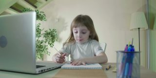 用笔记本电脑做作业。专注的小可爱的孩子在桌子上学习做家庭作业