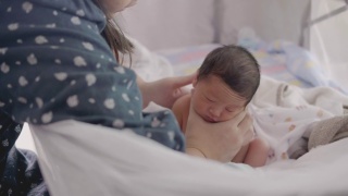 亚洲妈妈在给宝宝喂奶后，用奶瓶喂奶，帮助宝宝消化食物。视频素材模板下载