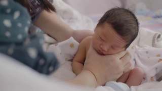 亚洲妈妈在给宝宝喂奶后，用奶瓶喂奶，帮助宝宝消化食物。视频素材模板下载