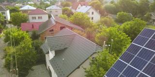 空中俯瞰的新现代住宅小屋与蓝色闪亮的太阳能光伏板系统屋顶。可再生生态绿色能源生产理念。