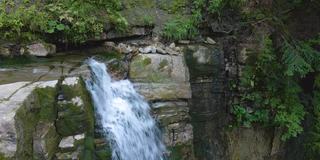 在夏季热带雨林中，美丽的瀑布在山河上，白色的泡沫水从岩石悬崖上落下