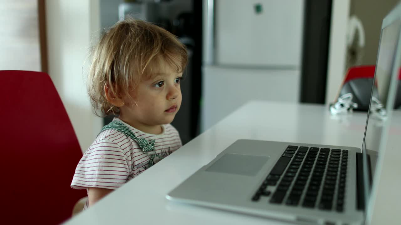 小男孩盯着笔记本电脑屏幕看媒体。婴儿看卡通片