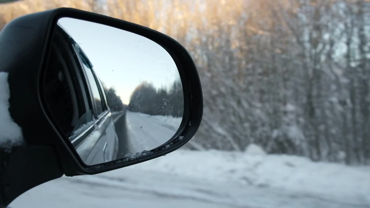 冬季森林道路的侧视镜反射。风景与空旷的高速公路穿过雪原森林。汽车在路上超速行驶。汽车在运动。旅游，旅行，旅行概念。冰雪覆盖的树木。